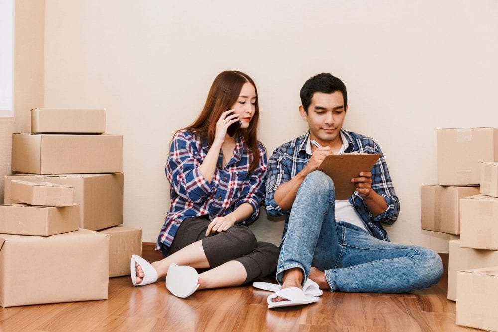 The Essential Checklist for Moving House Graphic to show young couple checklist with cardboard box at home - Business online and delivery concept