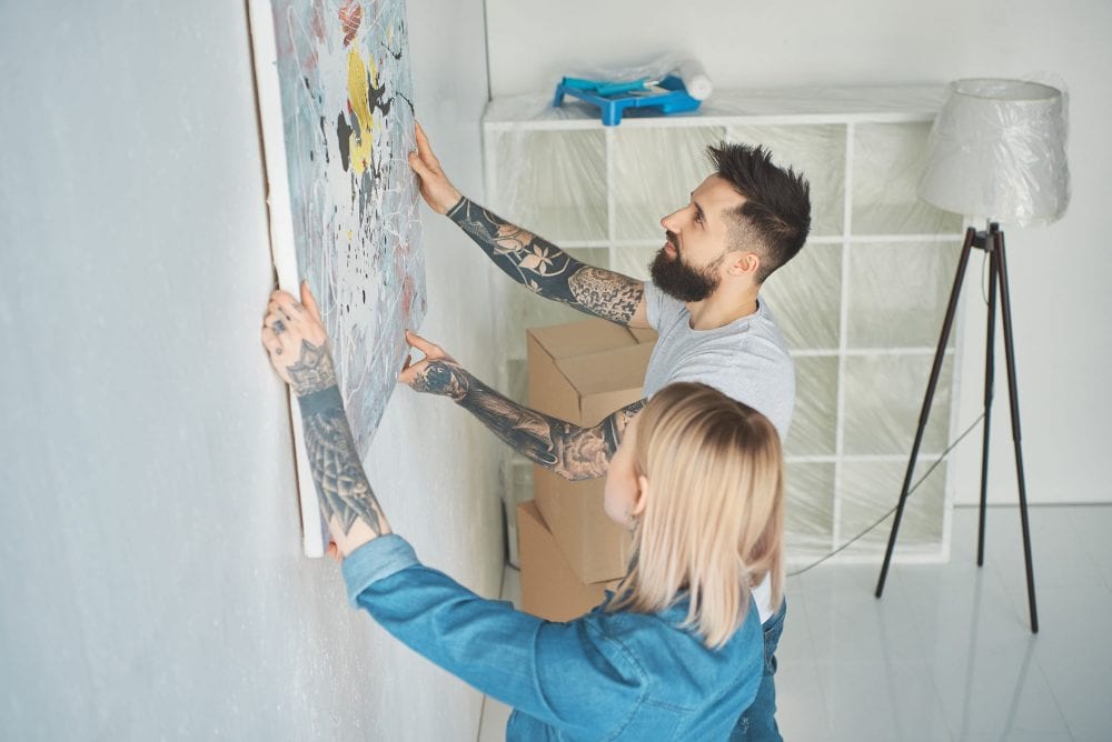 6 Quick Fix Ideas to Increase Your Property Value Graphic to show a young couple hanging a painting up in their new home